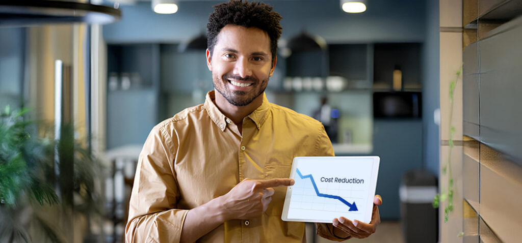 Man in a tan shirt presenting a tablet showing a downward cost-reduction chart in an office setting